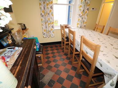 A dining room with wooden chairs around a table with a patterned tablecloth next to a window with patterned curtains in Carriguisnagh Ballycastle