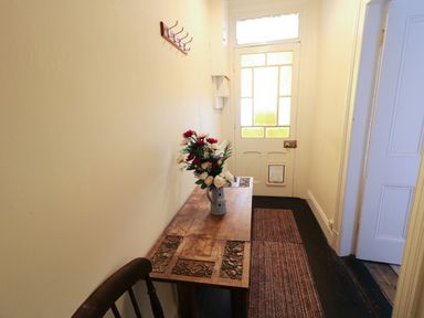A narrow hallway with a wooden table holding a vase of flowers a doormat and a white door at Carriguisnagh in Ballycastle