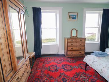 A bedroom with wooden wardrobe dresser bed red patterned carpet and windows at Carriguisnagh in Ballycastle