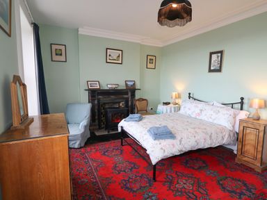 A bedroom with a bed towels on it a wooden dresser a blue armchair a fireplace and framed pictures on the walls at Carriguisnagh in Ballycastle