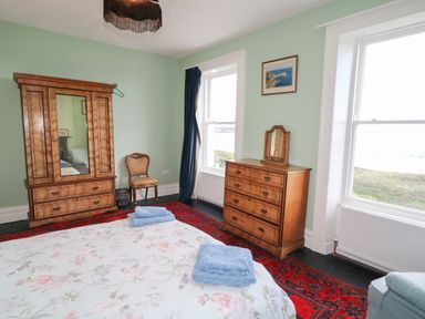 A bedroom with wooden wardrobe chest of drawers and chair by windows at Carriguisnagh in Ballycastle