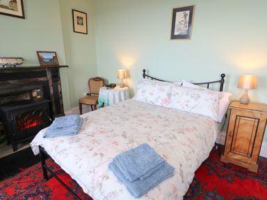 A bedroom with a bed with floral bedding and blue towels on a red rug with lamps on bedside tables and a fireplace at Carriguisnagh in Ballycastle