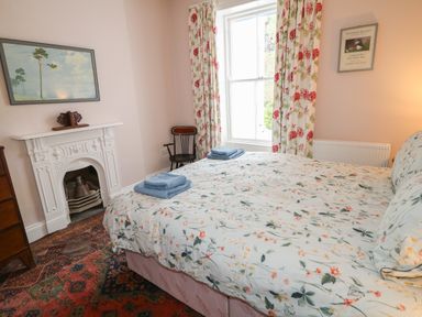 A bedroom with a bed covered in floral bedding folded towels a chair a fireplace a chest of drawers floral curtains a window and framed pictures on the walls at Carriguisnagh in Ballycastle