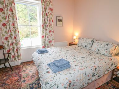 A bedroom with a large bed and floral bedding next to a window with floral curtains at Carriguisnagh in Ballycastle