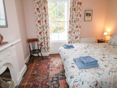 A bedroom with a bed covered in floral bedding and blue towels a wooden chair floral curtains and a patterned rug at Carriguisnagh in Ballycastle