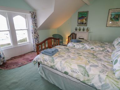 A bedroom with two single beds with leaf patterned bedding a green chair a small fireplace and large windows at Carriguisnagh in Ballycastle