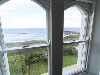 View of the ocean beach and greenery through a double arched window at Carriguisnagh in Ballycastle