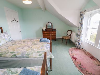 A bedroom with two single beds a wooden dresser a chair and a window with floral curtains at Carriguisnagh in Ballycastle