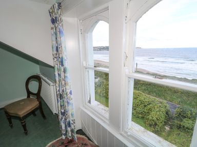 A room corner with a wooden chair a radiator floral curtains and a window overlooking a beach and sea at Carriguisnagh Ballycastle