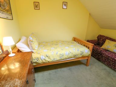 A bedroom with a wooden bed with yellow floral bedding a wooden dresser with a lamp and a patterned sofa at Carriguisnagh in Ballycastle