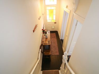 A narrow hallway with a wooden chair a table with flowers a rug on the floor and a door with stained glass panels at Carriguisnagh in Ballycastle