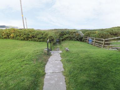 A concrete path with railings leading down between grassy areas to a gate surrounded by bushes at Carriguisnagh in Ballycastle