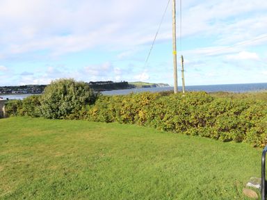 A grassy lawn with shrubs and bushes near the coastline with a view of cliffs and the sea at Carriguisnagh in Ballycastle