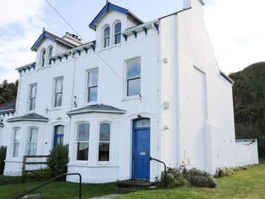 A white two-story house with blue doors and windows surrounded by grass at Carriguisnagh in Ballycastle