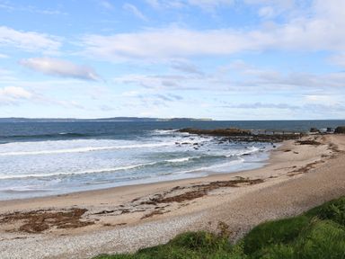 A sandy beach with seaweed and a rocky shoreline with waves and an ocean view at Carriguisnagh in Ballycastle