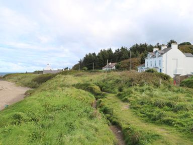 A coastal path with grassy banks leading to white houses near a forest at Carriguisnagh in Ballycastle