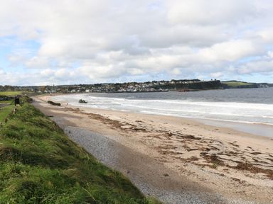 A sandy beach with seaweed and waves near a grassy area and a town with cliff in the background at Carriguisnagh Ballycastle