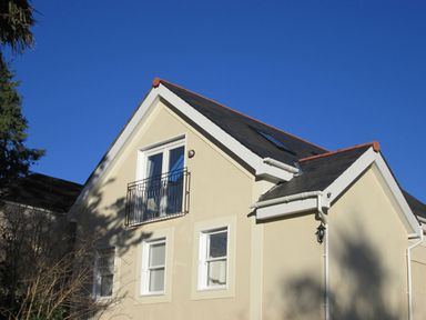 A two-story house with beige walls white window frames and a black roof under a clear blue sky at Monterey Mews in Torquay