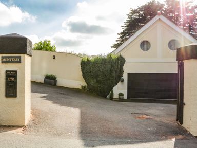 Driveway entrance with a mailbox on a wall and garage with circular windows at Monterey Mews in Torquay