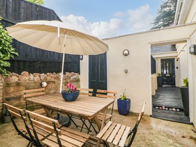 An outdoor patio with a wooden table and chairs under a large umbrella at Monterey Mews in Torquay