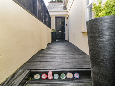 A front porch with a black door wooden decking and painted stones spelling welcome at Monterey Mews in Torquay