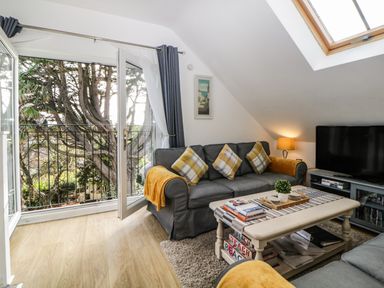 A living room with a gray sofa and yellow cushions a coffee table and an open door leading to a balcony at Monterey Mews in Torquay
