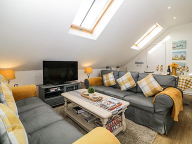 A living room with gray sofas and yellow cushions a coffee table and a television at Monterey Mews in Torquay