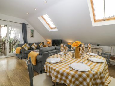 A living and dining area with a yellow checkered tablecloth on the table and gray sofas at Monterey Mews in Torquay