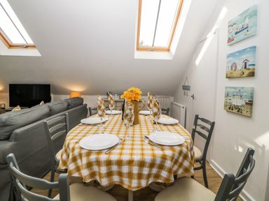 A dining table set with plates glasses and napkins in a room with skylights and a sofa at Monterey Mews in Torquay