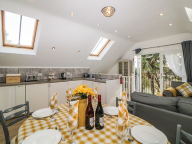 A dining table set with plates glasses napkins and wine bottles near a kitchen with skylights and a living area with sofas and a glass door at Monterey Mews in Torquay