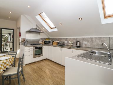 A kitchen with white cabinets a stove a microwave a toaster a kettle and a dining table with chairs at Monterey Mews in Torquay