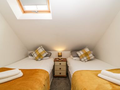 A small bedroom with two single beds with mustard blankets and plaid pillows and a nightstand with a lamp between them at Monterey Mews in Torquay
