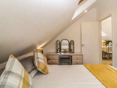 A bedroom with a bed with yellow and gray cushions and a dressing table with mirrors at Monterey Mews in Torquay
