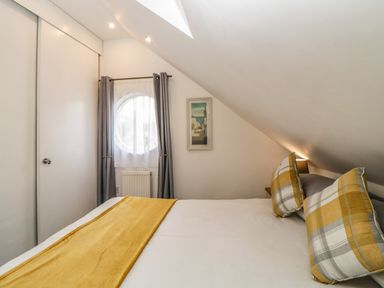 A bedroom with a bed featuring yellow and gray plaid pillows and a yellow runner near a round window with gray curtains at Monterey Mews in Torquay