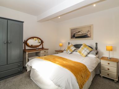 A bedroom with a bed yellow throw pillows bedside tables lamps wardrobe and dressing table Monterey Mews Torquay
