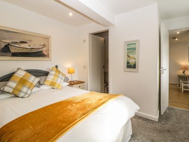 A bedroom with a bed with yellow and white pillows a bedside table with a lamp and two open doors at Monterey Mews in Torquay