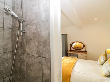 A bathroom shower with tiled walls next to a bedroom with bed a wooden dressing table and pillows at Monterey Mews in Torquay