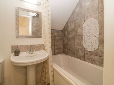 A bathroom with a sink and mirror and a bathtub with tiled walls at Monterey Mews in Torquay
