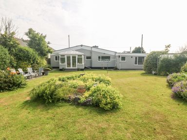 A garden with lawn chairs and a table on the left side and a circular flower bed in the middle in front of a single story house at Little Mead in Trearddur Bay