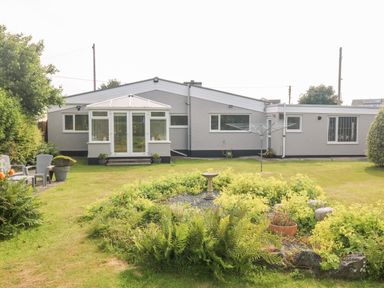 A single-story house with a garden and patio furniture in front at Little Mead in Trearddur Bay
