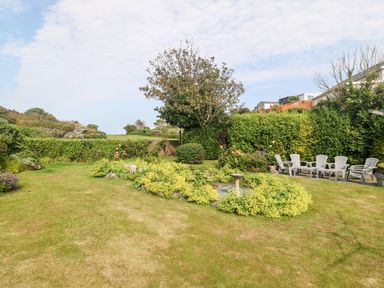 A garden with grass lawn shrubs and outdoor chairs at Little Mead in Trearddur Bay