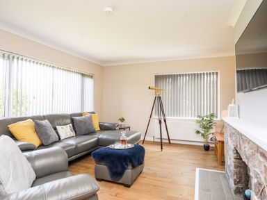 A living room with a grey leather sofa and armchair a telescope and a stone fireplace at Little Mead in Trearddur Bay