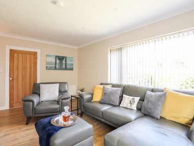 A living room with grey leather sofas and yellow and grey cushions at Little Mead in Trearddur Bay