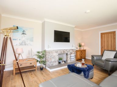 A living room with a wall-mounted TV fireplace wooden cabinets telescope and gray leather furniture at Little Mead in Trearddur Bay