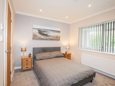 A bedroom with a double bed two bedside tables with lamps and a window with vertical blinds at Little Mead in Trearddur Bay