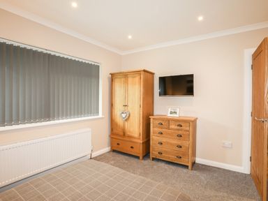 A bedroom with a bed a wooden wardrobe a wooden chest of drawers and a wall-mounted TV at Little Mead in Trearddur Bay