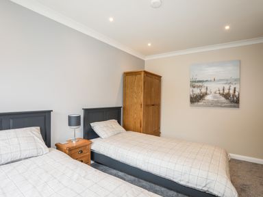A bedroom with two single beds a wooden wardrobe a bedside table with a lamp and a painting on the wall at Little Mead in Trearddur Bay