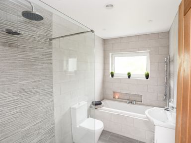 A bathroom with a shower area bathtub toilet sink and three potted plants on the window ledge at Little Mead in Trearddur Bay