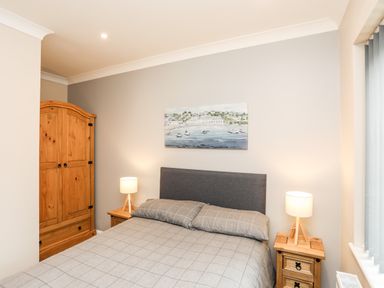 A bedroom with a double bed bedside tables with lamps a wooden wardrobe and painting on the wall at Little Mead in Trearddur Bay