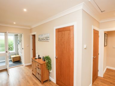 Hallway with wooden doors wooden floor a wooden cabinet and an open door leading outside at Little Mead in Trearddur Bay